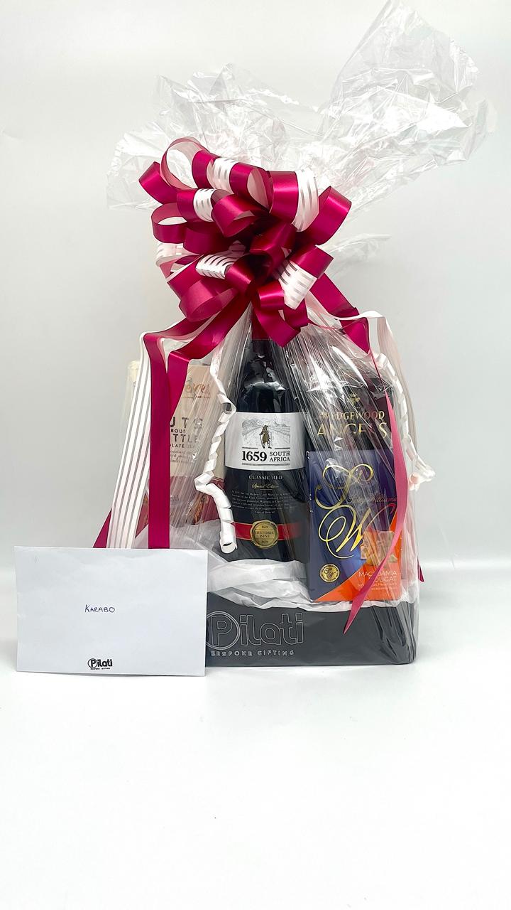A luxury gift basket containing a large magenta and white striped bow, with a white card in front.