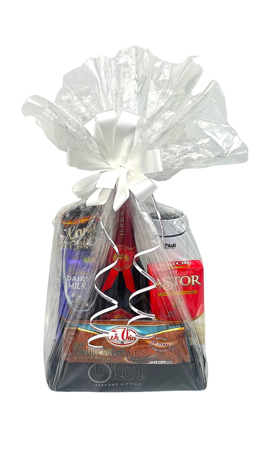 A gourmet gift basket wrapped in clear love and tied with a white ribbon, containing a bottle of cola, a red packaged item, and a chocolate bar, on a white background.
