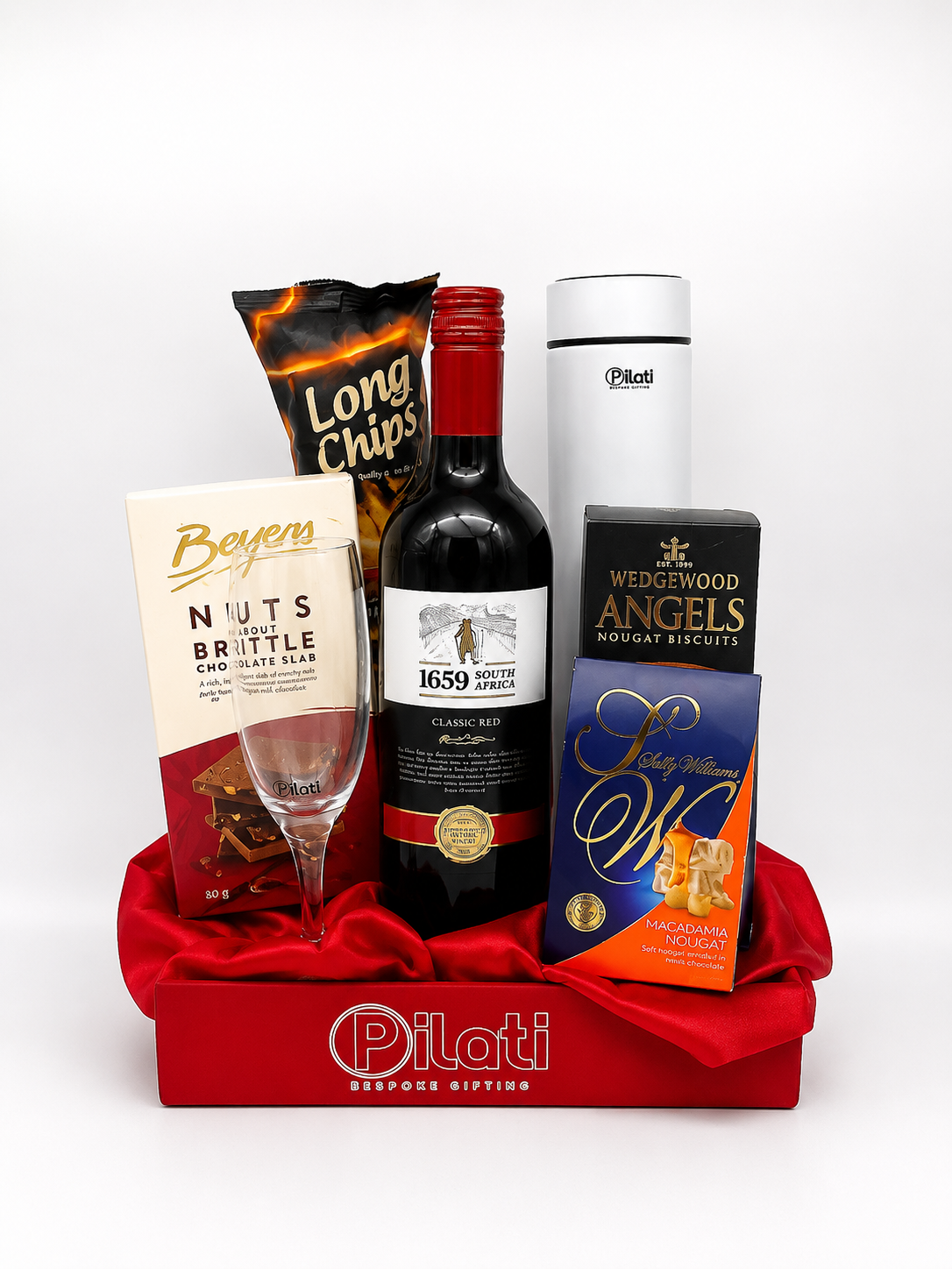 A Pilati curated gourmet gift basket featuring a bag of Long Chips, a box of Wedgewood Angels Biscuits,  a glass, and a white thermos, all arranged in a red satin-lined tray on a white background.